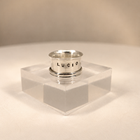 Silver ring on a clear stand with 'Lucio' branding against a beige background