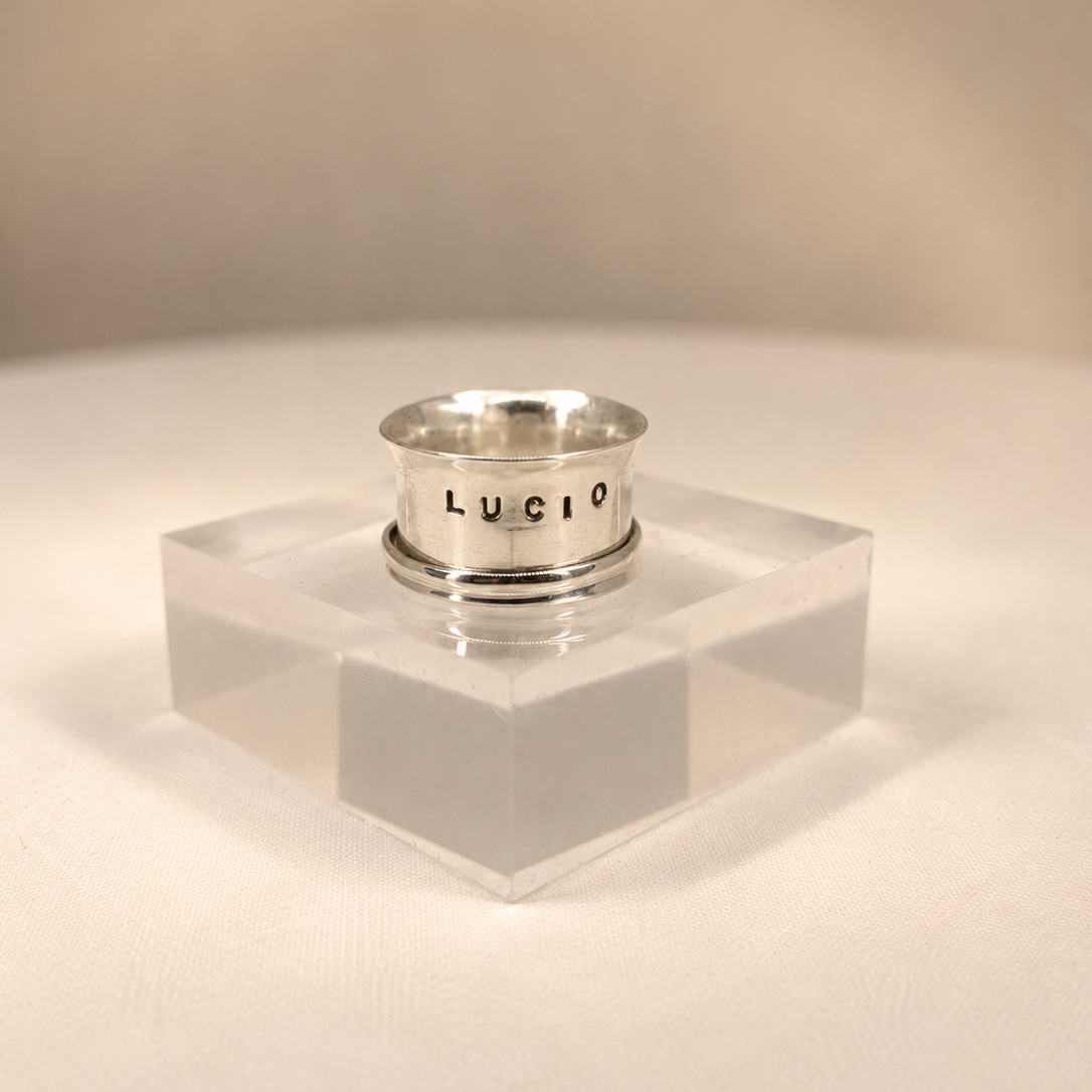 Silver ring on a clear stand with 'Lucio' branding against a beige background