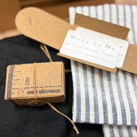 A close-up of a kraft card box and a blue-and-white striped fabric, all arranged on a dark fabric.