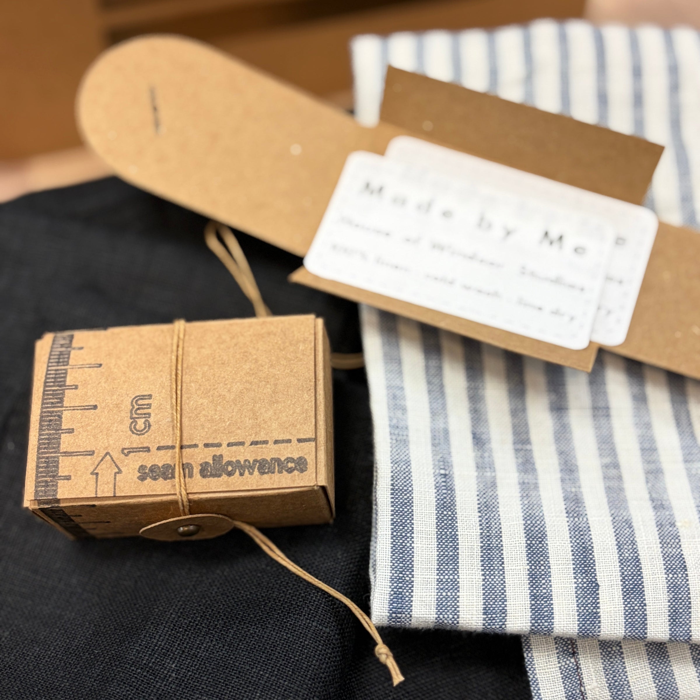 A close-up of a kraft card box and a blue-and-white striped fabric, all arranged on a dark fabric.